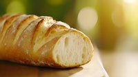 Fresh crusty baguette with soft white crumb interior on wooden surface against blurred natural background, close-up view showing texture and layers.