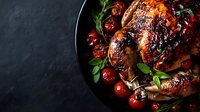 Roasted whole chicken with caramelized cherry tomatoes, fresh herbs and balsamic glaze served on black plate against dark background, moody food photography.