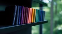 Row of colorful book spines arranged in rainbow spectrum order on dark shelf against blurred green natural background, creating minimalist library aesthetic.