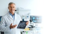 Senior male doctor in white coat holding brain scan in modern medical laboratory with microscope and equipment for neurological diagnosis and healthcare research.