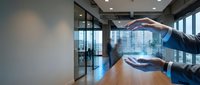 Business protection concept with hands creating shield gesture over modern office conference room with glass walls and city view.