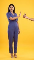 Young South Asian businesswoman in purple suit refusing cigarette offer with stop gesture on yellow background for health awareness campaigns.