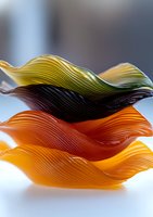 Colorful wavy glass bowls stacked in yellow, black, and orange tones showing elegant rippled texture and translucent surfaces with soft lighting effect.