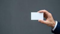 Male hand holding blank white business card against gray background, suitable for corporate branding and professional mockup designs.