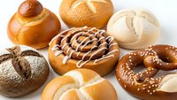 Assorted fresh baked bread rolls, pretzels and pastries on white background. Variety of artisan bakery products including sourdough, sesame seed buns and sweet treats.