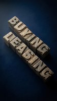 Wooden letterpress blocks spelling "breaking" and "bearing" arranged diagonally on deep blue surface, casting shadows. Vintage typography and printing concept.
