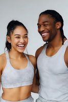 Young diverse couple laughing together while wearing athletic wear, sharing genuine moment of joy against white background. Perfect for wellness and lifestyle content.