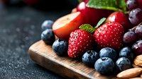 Fresh mixed berries and fruits on wooden cutting board with water drops. Dark moody background creates appetizing contrast for food photography and healthy eating concept.