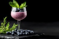 Fresh blueberry smoothie cocktail garnished with mint leaves and berries in elegant glass on dark slate background with copy space.