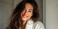 Young Hispanic woman with long brown hair smiling joyfully in soft natural light wearing white sweater. Authentic happiness and positive emotions lifestyle portrait.