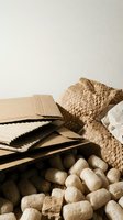 Sustainable packaging materials including corrugated cardboard, woven basket and biodegradable packing peanuts on neutral background for eco-friendly shipping.