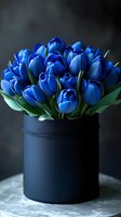 Vibrant blue tulips arranged in black cylindrical vase against dark background. Fresh spring flowers create elegant floral composition for luxury interior decor.