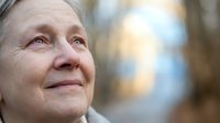 Senior woman with fair skin and light hair gazing upward outdoors with blurred background, expressing hope, contemplation, and peaceful emotion for wellness and lifestyle content.