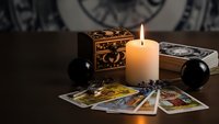 Mystical fortune telling setup with burning candle, tarot cards spread on wooden table, ornate box and crystal spheres for divination readings.