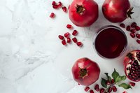 Fresh pomegranates and juice on marble background, with scattered arils and cut fruit revealing juicy seeds.
