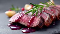 Juicy sliced medium rare beef steak with fresh rosemary and red wine sauce on dark stone background, close up view of grilled meat preparation.
