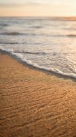 Soft waves gently wash onto golden sandy beach at sunset, creating a serene coastal scene perfect for travel, relaxation, and wellness design projects.