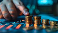 Stacked gold coins on financial chart with blurred hand in background showing declining trend, dramatic lighting with blue and orange tones for business concept.