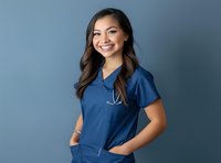 Young Asian female healthcare worker in blue scrubs with stethoscope smiling confidently against blue studio background. Professional medical staff portrait.