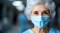 Elderly Caucasian woman wearing protective surgical face mask in medical facility, looking directly at camera with serious expression and gray hair.