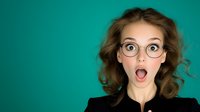 Young woman with curly hair and round glasses showing surprised expression with open mouth against turquoise background. Concept of amazement and shock.