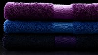 Stack of folded cotton bath towels in purple, blue and black colors on dark background with soft side lighting creating luxurious spa atmosphere.