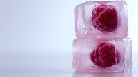Red raspberry frozen in clear ice cubes on light background, refreshing summer drink garnish for cocktails and beverages.