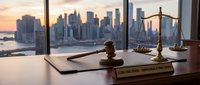 Legal office desk with gavel and scales of justice overlooking city skyline at sunset. Corporate law firm workspace for attorney consultation services.