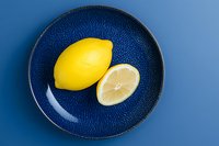 Fresh lemon whole and sliced on a blue ceramic plate against a blue background, showcasing vibrant color contrast for food and lifestyle use.