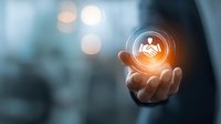 Businessman holding glowing virtual handshake icon, symbolizing partnership and business agreement in modern corporate environment with bokeh background.