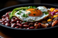 Vibrant breakfast bowl with sunny side up egg, red beans, grilled carrots, avocado and fresh herbs served on black plate against dark background. Food photography.