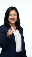 Confident Hispanic businesswoman in navy suit pointing at camera with finger gesture on white background for corporate marketing materials.