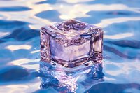 Crystal clear ice cube floating in blue rippling water with pink and purple reflections creates mesmerizing light effects and abstract patterns.