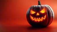 Spooky carved jack-o-lantern pumpkin with glowing orange face on red background for Halloween decorations and seasonal autumn celebrations.