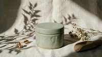 Sage green round cosmetic jar with lid on neutral linen fabric with botanical shadows and dried flowers for natural skincare packaging mockup.