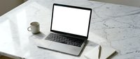 Modern laptop with blank white screen on marble desk workspace with coffee cup and notebook for business presentations and mockup designs.