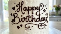 Happy Birthday text with decorative swirls and stars hand-lettered on cream fondant cake, suitable for celebration designs and greeting cards.
