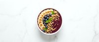 Acai smoothie bowl topped with granola, blueberries and banana slices on marble surface for healthy breakfast and superfood nutrition concepts.