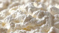 Fresh whipped cream texture with soft peaks and valleys in creamy white color, macro photography showing delicate details and light shadows.