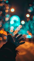 Silhouetted hand reaching towards glowing turquoise and orange bokeh lights creating magical nighttime atmosphere with dreamy blurred background for creative photography.