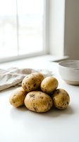 Fresh organic potatoes with soil on white kitchen counter near window with natural light for healthy cooking and farm to table meals.