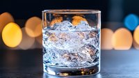 Whiskey or bourbon with ice cubes in a rocks glass against blurred warm and cool bokeh lights, suitable for beverage, bar, and hospitality marketing.