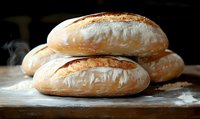 Fresh baked artisan sourdough bread loaves with crispy golden crust and flour dusting on rustic wooden surface, steam rising in dark background.