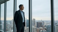 Professional businessman in dark suit standing by floor-to-ceiling windows overlooking urban cityscape, contemplating future business opportunities and success.