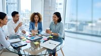Diverse business team collaborating in modern office meeting room with city view. Professional women and men discussing strategy at conference table.