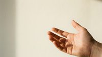 Open hand reaching forward in warm natural light with soft shadows on neutral beige wall background for presentation and offering concepts.