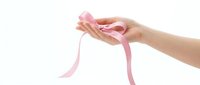 Female hands holding pink ribbon symbol for breast cancer awareness campaign and women health support on white background.