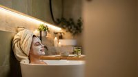 Relaxed woman enjoying spa bath with towel on head, candles and herbal tea creating peaceful wellness atmosphere for self-care and relaxation at home.