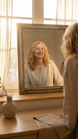 Happy middle-aged blonde woman smiling at her reflection in vintage mirror during morning routine in bright sunlit bathroom with natural lighting.