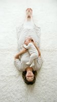Young Caucasian mother lying on soft white carpet holding sleeping newborn baby on her chest, aerial top view, tender bonding moment.